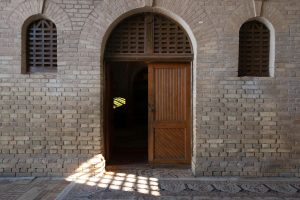 An inviting open wooden doorway within a historic brick arched wall, capturing shadows and ambiance.